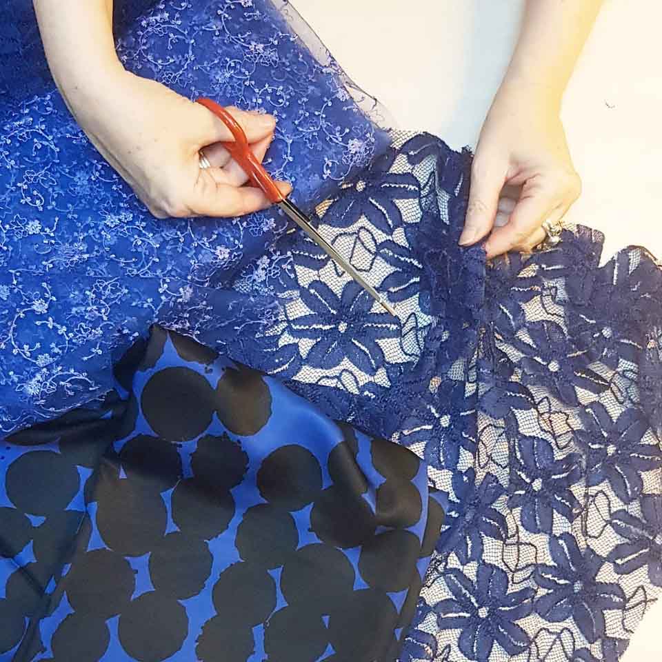 Handen van ontwerpster Claudia Träumer die met een schaar exclusieve blauwe stoffen en fijn kant knipt voor het maken van kleding op maat in het CLAU-D atelier in Arnhem