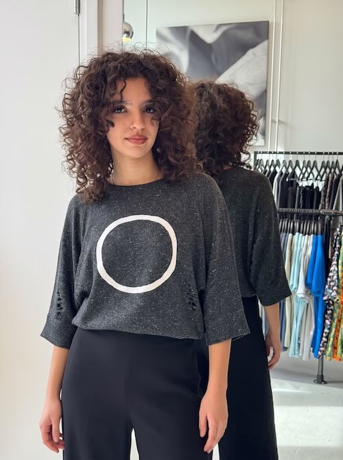 Vrouw in de antracietgrijze Silk Circle Grey sweater van zijde en wol met ecru cirkel, gedragen op een zwarte wijde broek met hoge taille